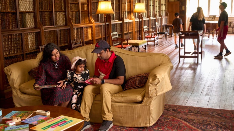 A family in the Long Gallery at Blickling Hall reading books on the sofa, other visitors explore in the background